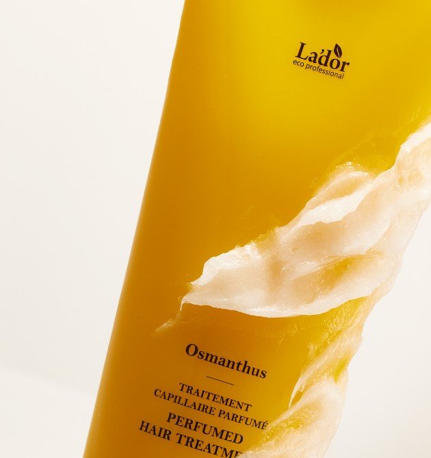 Close-up of golden-yellow hair treatment tube with creamy texture swirled on its surface against a light background
