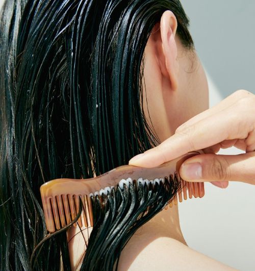 Hand combing wet, glossy hair with a brown wide-tooth comb focusing on smooth, moisturized strands.
