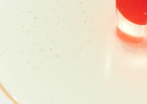 Close-up of a glossy clear liquid drop with an orange cap implying scalp cleansing shampoo texture on light surface