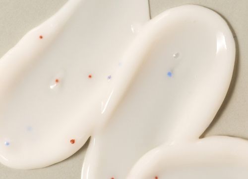 White creamy scalp treatment with small red and blue exfoliating beads spread on a smooth surface