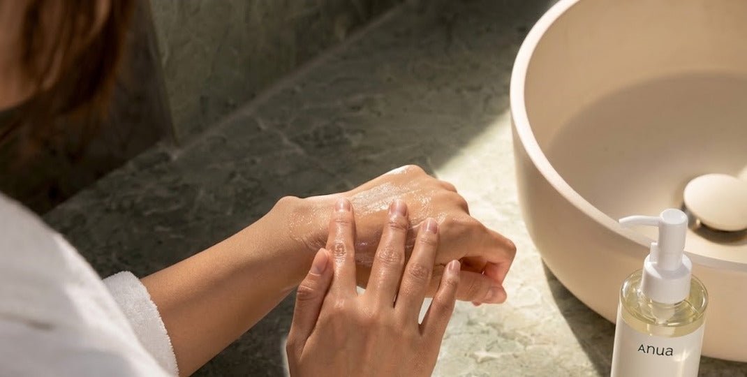 Hands rubbing together beside a bowl and clear pump bottle on a stone bathroom counter
