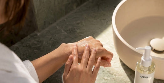 Hands rubbing together beside a bowl and clear pump bottle on a stone bathroom counter