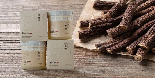 Four beige jars and boxes arranged beside dried licorice roots on a weathered wooden surface