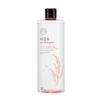 Clear bottle of mild cleansing water with pink rice grain illustration and black cap on white background