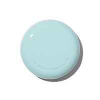 Round pastel blue powder cushion compact with subtle embossed lettering on clean white background