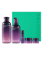 Set of purple gradient skincare bottles and jars arranged in front of bright green box with brand name visible
