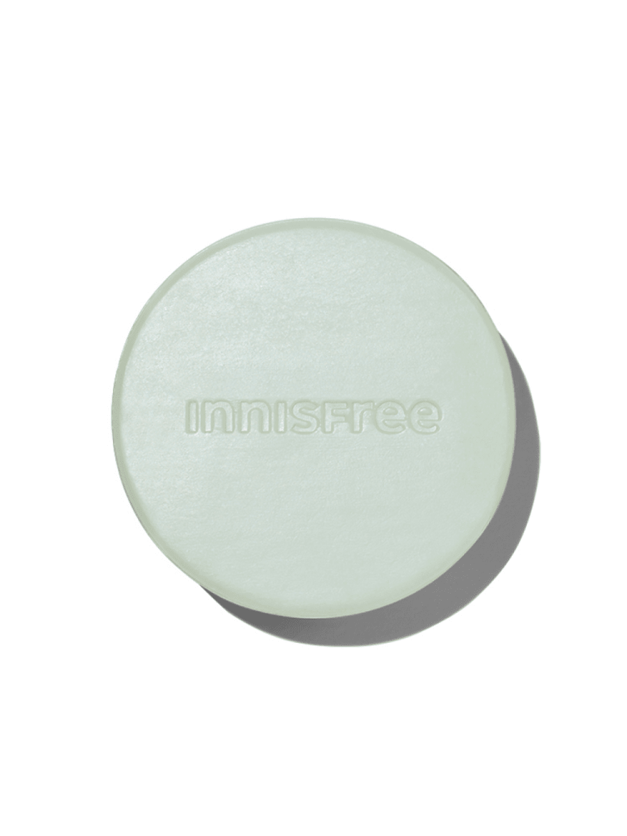 Round pale green shampoo bar embossed with subtle brand name and soft shadow on white background