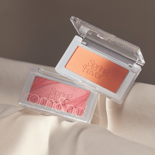 Two rectangular makeup compacts in coral and peach shades labeled Spring Fever on soft beige fabric background