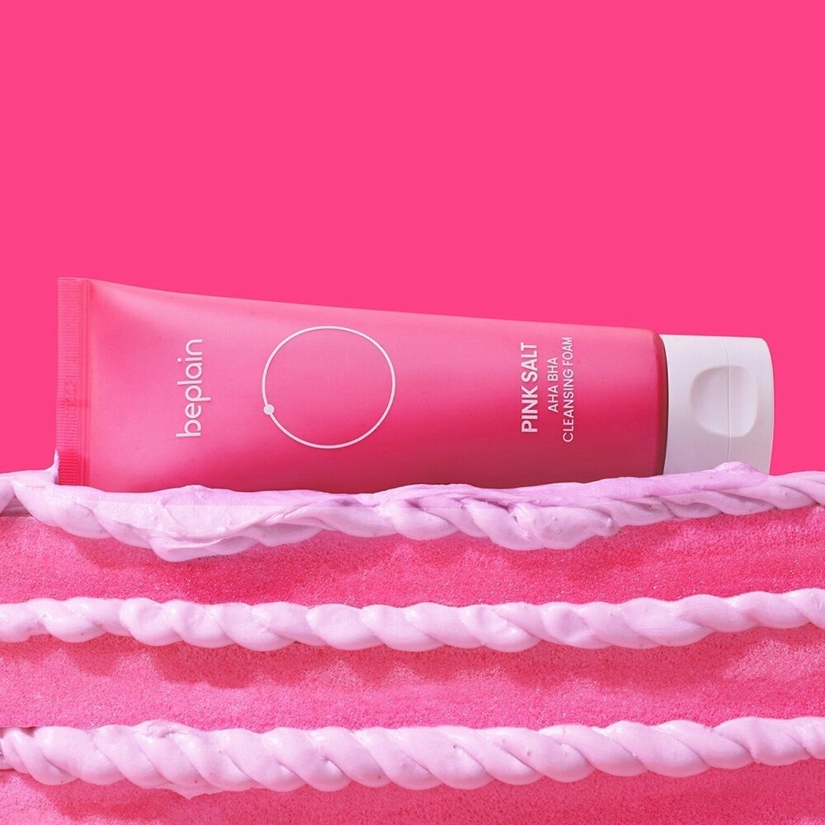beplain Pink Salt AHA BHA Cleansing Foam 120ml tube on bright pink background emphasizing exfoliation benefits