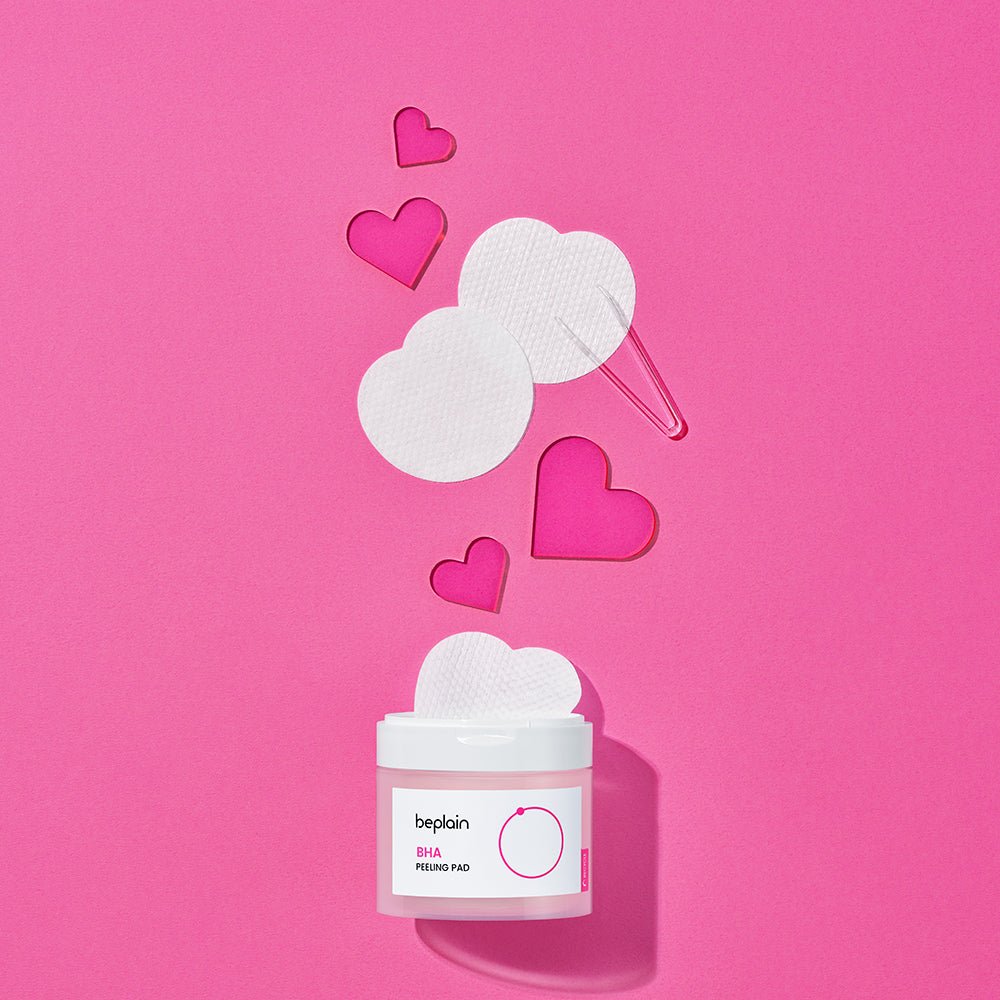 beplain BHA Peeling Pad 50P jar with round textured pads and pink acrylic heart shapes on vibrant pink background for gentle exfoliation