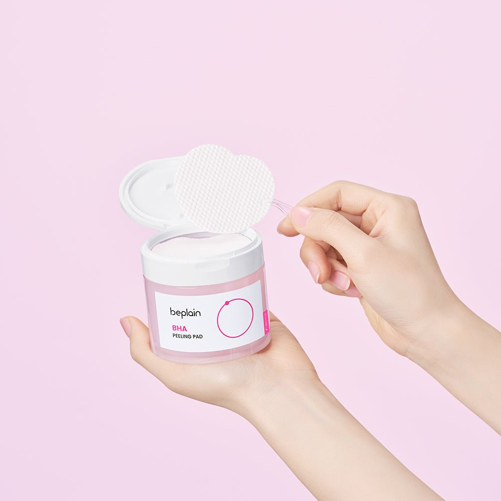 beplain BHA Peeling Pad 50P in clear pink jar held with textured pad lifted on tweezer against pink background