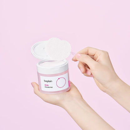 beplain BHA Peeling Pad 50P in clear pink jar held with textured pad lifted on tweezer against pink background