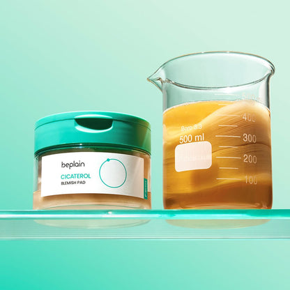 beplain Cicaterol Blemish Pads 70 sheets container with teal lid next to a glass beaker of amber liquid showing cooling effect