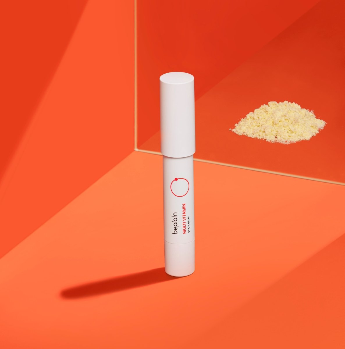 beplain Multi Vitamin Stick Balm 2.9g standing on orange surface with bright vitamin powder reflection nearby