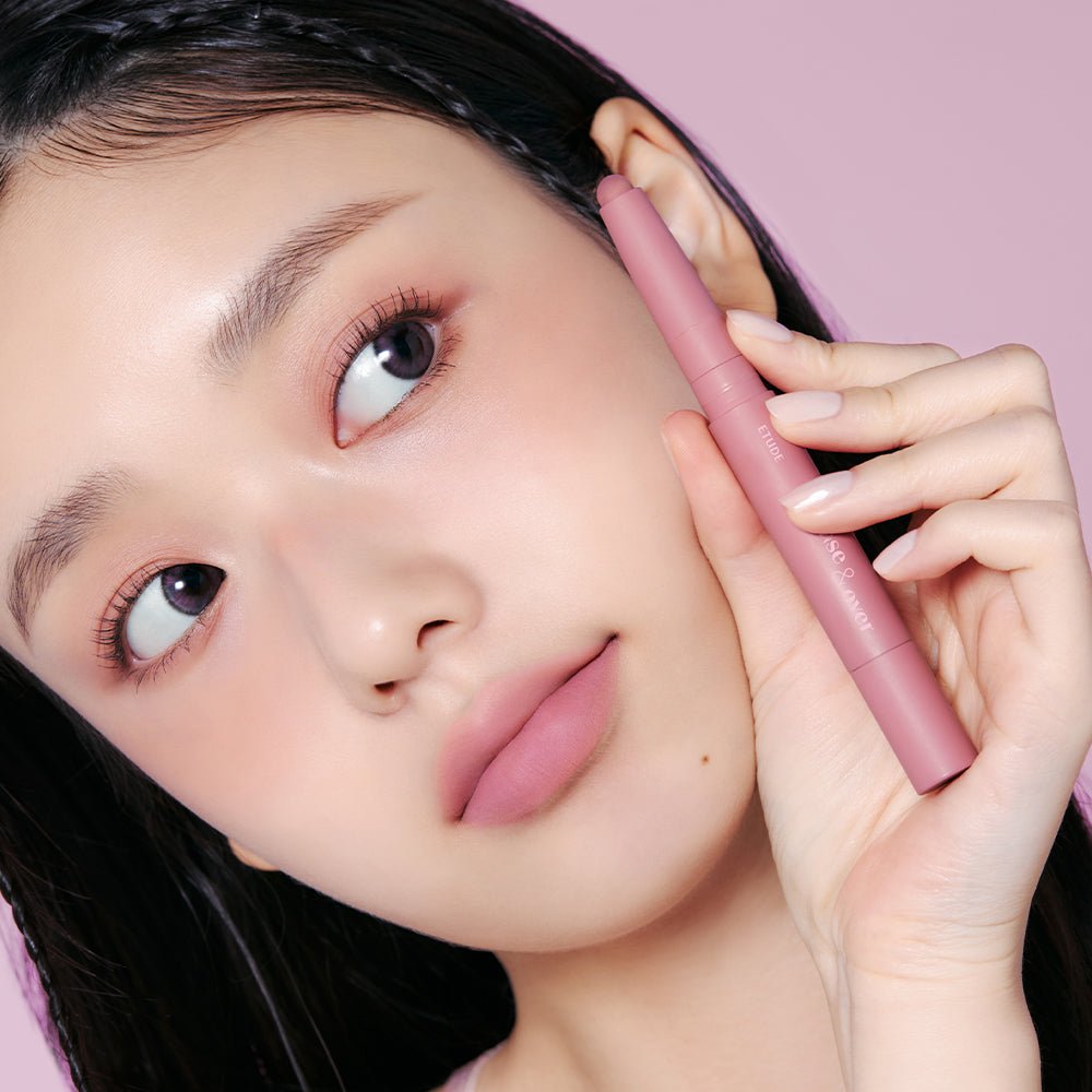 Model holding ETUDE Base & Over Lip Pencil #Pink Beige 1g close to face with soft pink makeup and enhanced definition