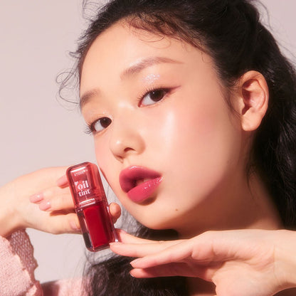 Model holding ETUDE Dear Darling Oil Tint 4.2g with glossy deep pink lip color and radiant skin close-up