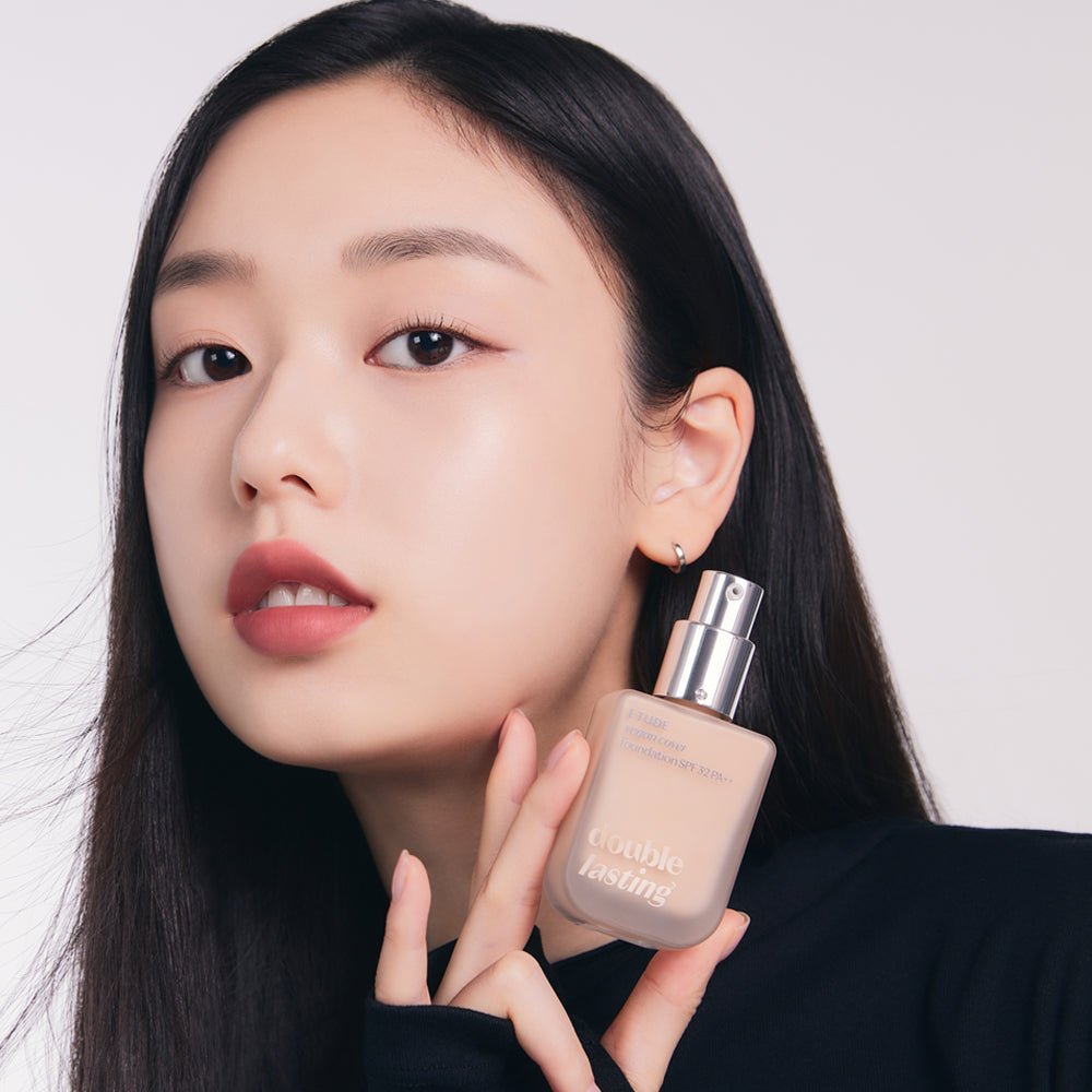 Model with flawless skin holding ETUDE Double Lasting Vegan Cover Foundation SPF32/PA++ 30g bottle with pump dispenser close-up