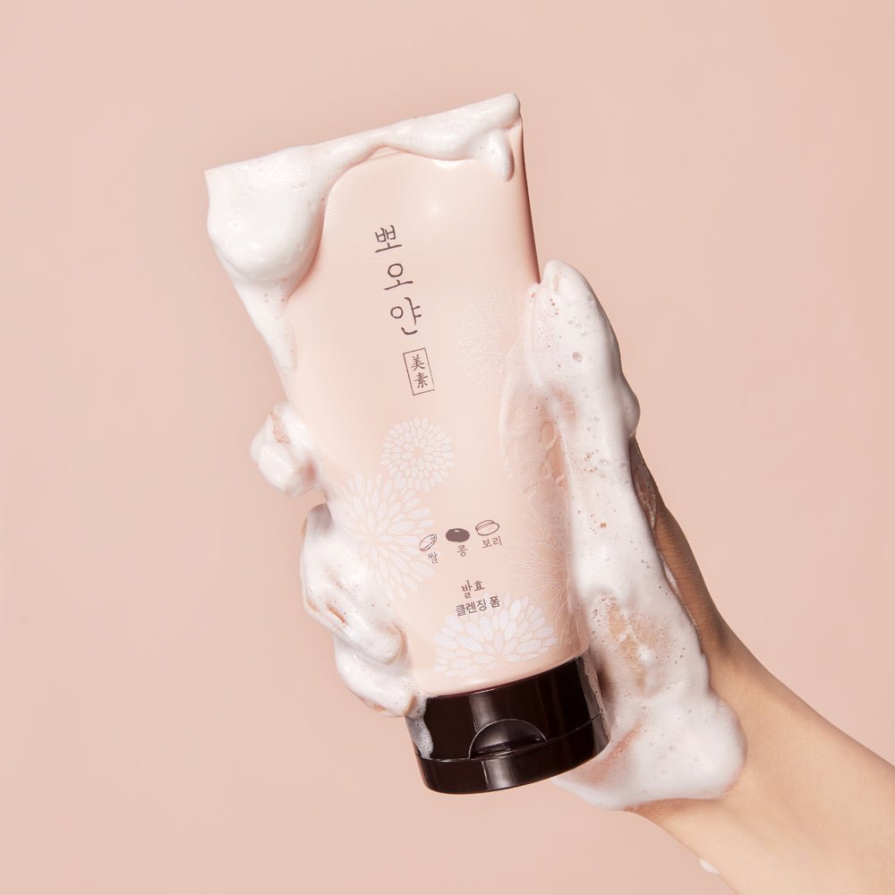 Hand holding ETUDE PPOYAN Cleansing Foam 150ml tube covered in gentle white foam on beige background