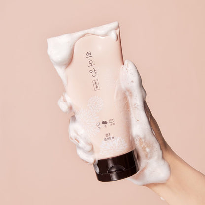 Hand holding ETUDE PPOYAN Cleansing Foam 150ml tube covered in gentle white foam on beige background