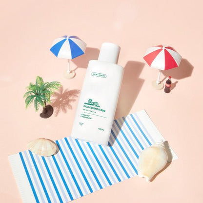 VT Cica Essence Sun 100ml SPF50+/PA++++ bottle on a striped towel with seashells, mini umbrellas, and a small palm tree model