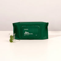 VT Cica Mild Cleansing Tissue 50pcs, 240g in dark green pack with thorough makeup removal beside a small glass with leaves