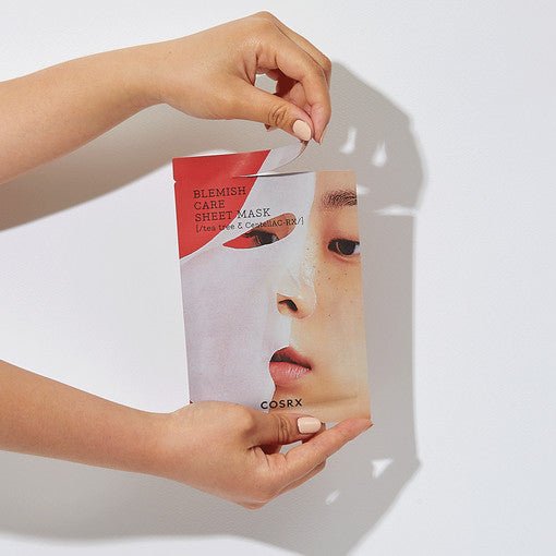 Hands holding a blemish care sheet mask package featuring a side profile of a woman’s face and red accents