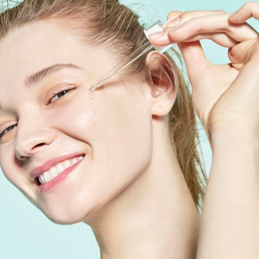Woman applying hydrating serum drop from dropper onto glowing, fresh skin with a light blue background