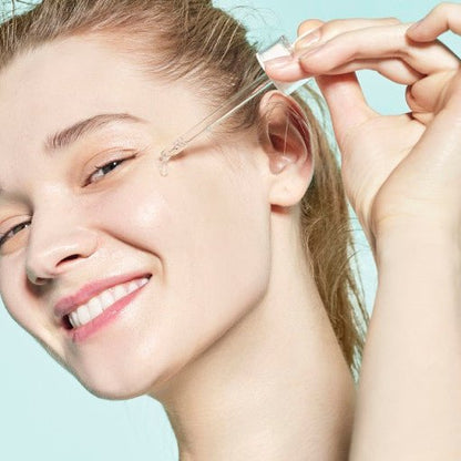 Woman applying hydrating serum drop from dropper onto glowing, fresh skin with a light blue background