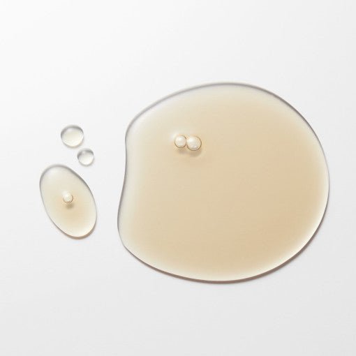 Light beige serum droplets with smooth texture on a white surface highlighting brightening skin care effect