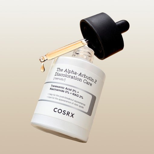 Bottle of brightening discoloration care serum with dropper releasing a golden liquid drop over beige background