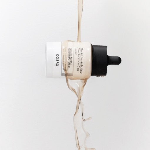 Dropper bottle of brightening serum with liquid pouring over, highlighting discoloration care benefits