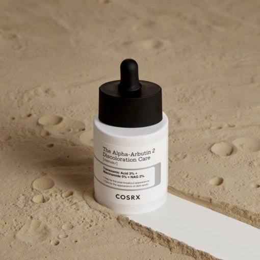 White serum bottle with black dropper cap resting on textured beige surface, highlighting brightening skincare benefit