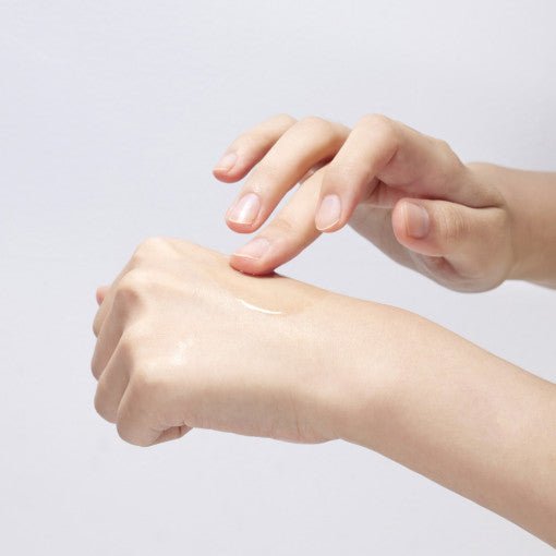 Person gently applying clear serum on the back of their hand showcasing smooth, hydrated skin texture
