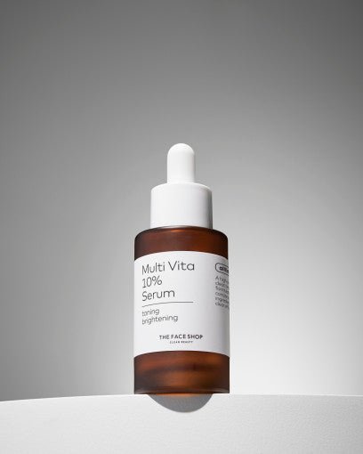 Brown glass dropper bottle of Multi Vita 10% serum with white label emphasizing brightening effect on gray background