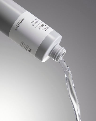 Clear liquid pouring from sleek white bottle labeled for texture improvement and brightening care on gray background