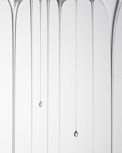 Multiple clear serum droplets stretching in thin vertical streams against a white background