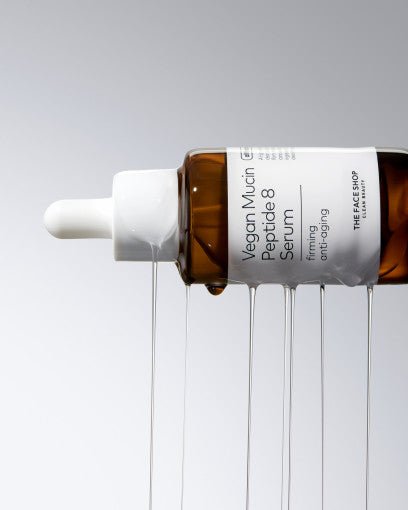 Amber dropper bottle of vegan mucin peptide serum with clear liquid dripping against gray background