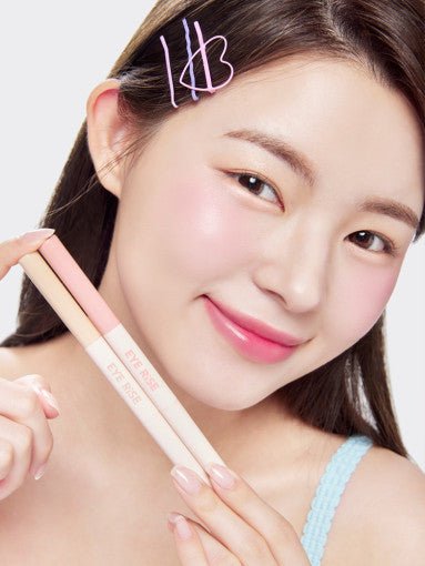 Young woman with clear skin holding dual-ended under eye makeup with soft pink and beige tones