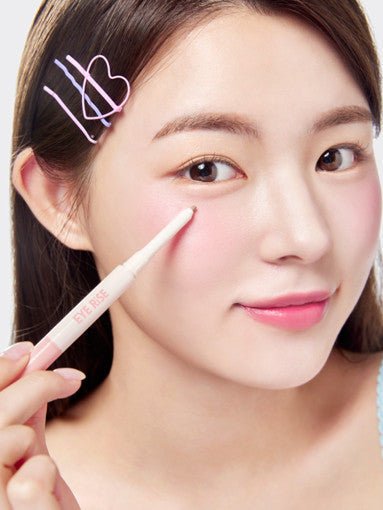Young woman applying precise under-eye makeup with a slim light pink pen applicator on fair skin