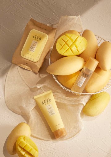 Soft cleansing wipes pack and tube of skincare product displayed with whole and sliced mangoes on light fabric background