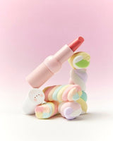 Pink-tinted lipstick with semi-gloss texture balanced on colorful twisted marshmallows against pink background