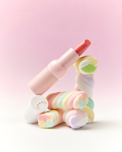 Pink-tinted lipstick with semi-gloss texture balanced on colorful twisted marshmallows against pink background