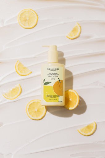Pump bottle of lemon verbena body lotion surrounded by fresh lemon slices on cream textured surface