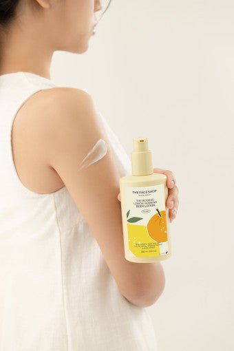 Person applying pale yellow lotion from pump bottle with lemon graphic on label to upper arm