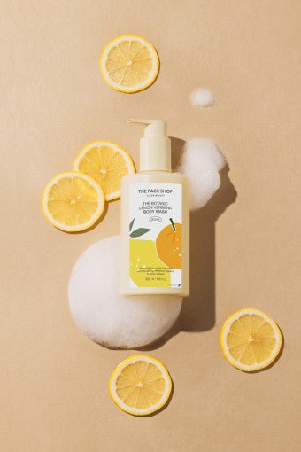 Pump bottle of hydrating lemon verbena body wash surrounded by lemon slices and foam on beige surface