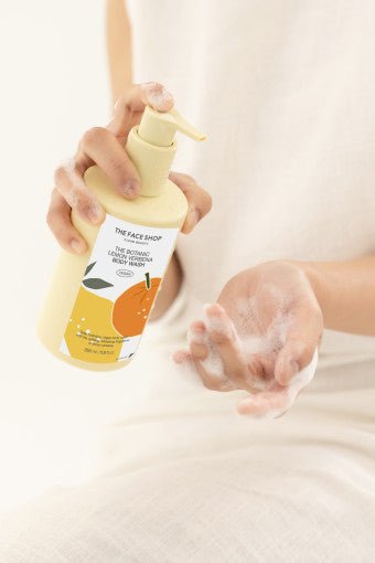 Person dispensing foamy lemon-scented body wash from pale yellow pump bottle onto hand