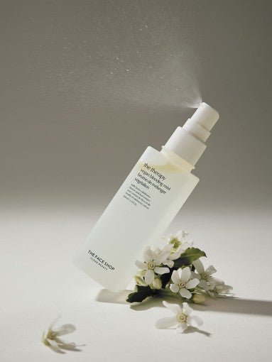 Frosted spray bottle releasing fine mist with white blossoms on neutral surface emphasizing moisture delivery