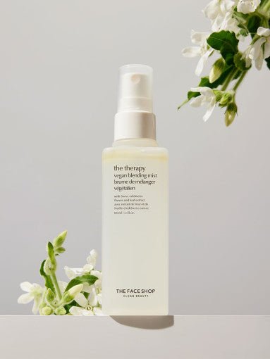 Spray bottle of vegan blending mist with white flowers in soft natural light on neutral background