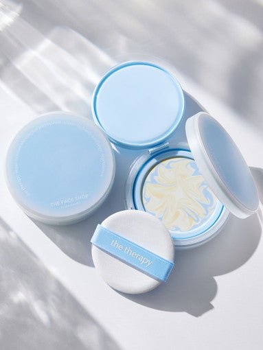 Open and closed blue compact cases with swirled sun pact and applicator puff on white surface with light shadows