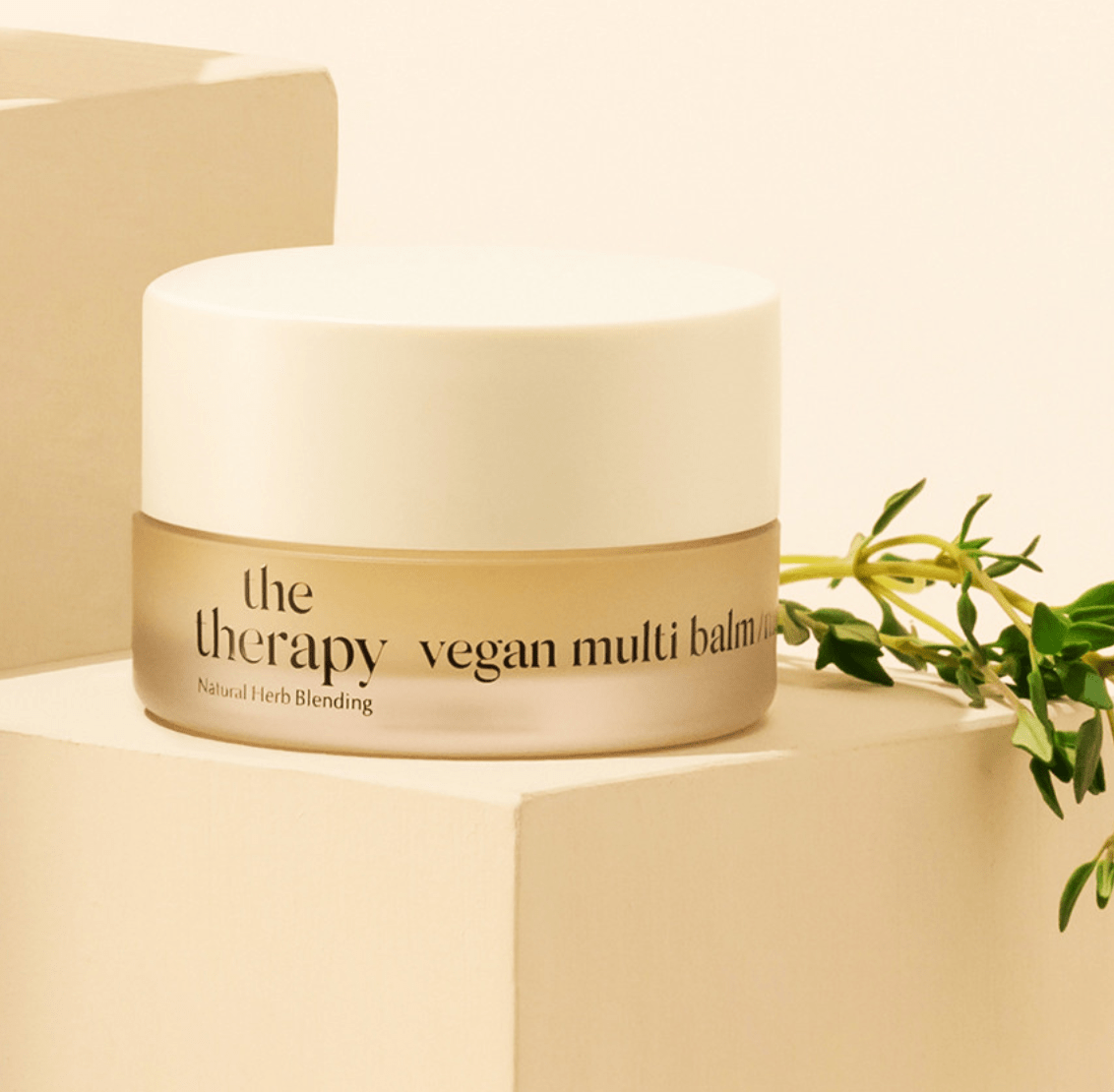 Frosted jar of moisturizing vegan multi balm with beige lid beside green herb sprig on neutral background